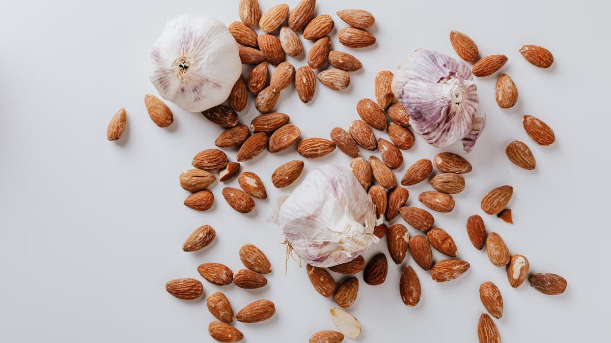 Top view of pile of raw partially peeled almonds and whole garlic bulbs with dry husk on white surface